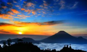 “Sunrise over the Dieng Plateau in Indonesia, with golden sunlight illuminating misty hills, volcanic craters, and scattered clouds.”